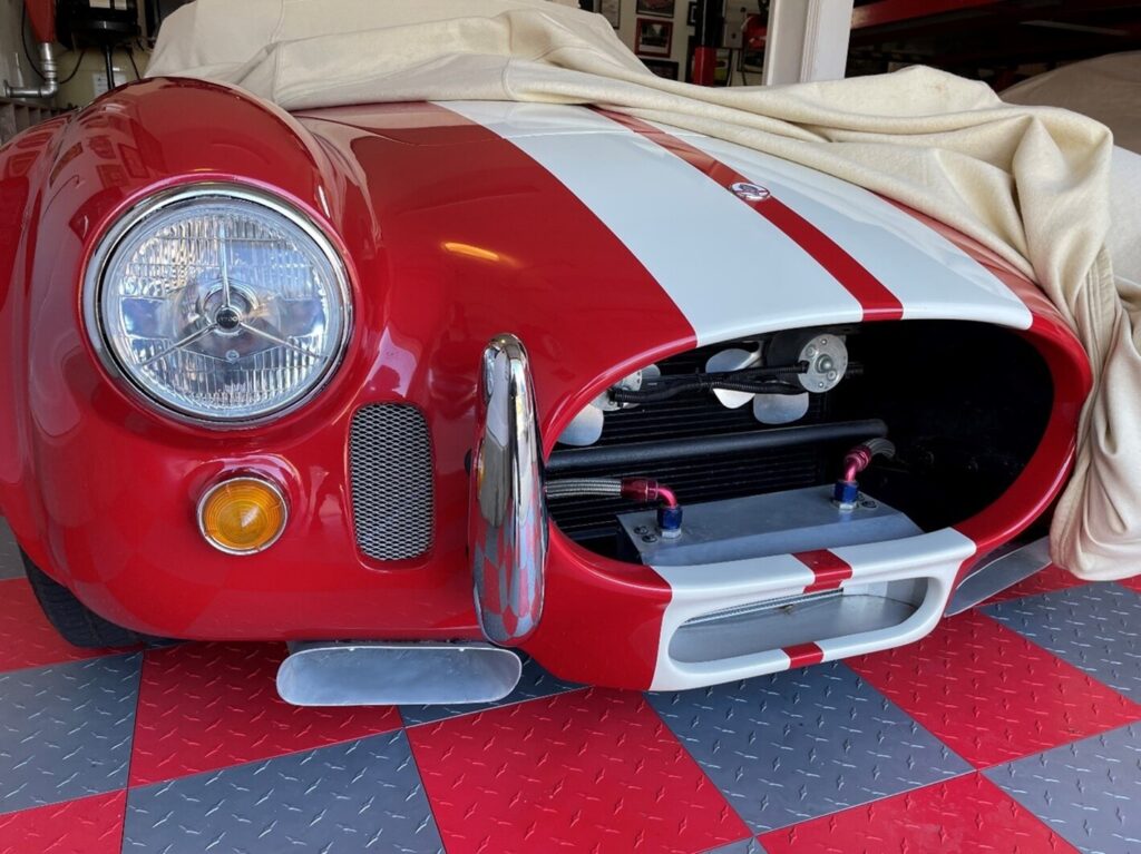A car cover partially removed from a red and white Cobra in a garage in preparing your classic car for driving
