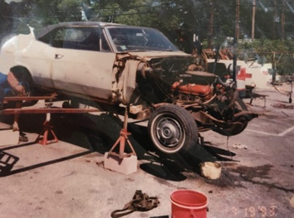 A beige convertible 1965 Chevy Impala on jack stands with front of the car removed as part of the classic car DIY restoration process