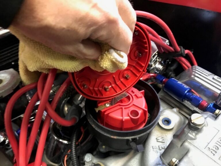 A mechanic cleaning the inside of a Ford distributor cap with a rag as part of maintaining a classic car engine