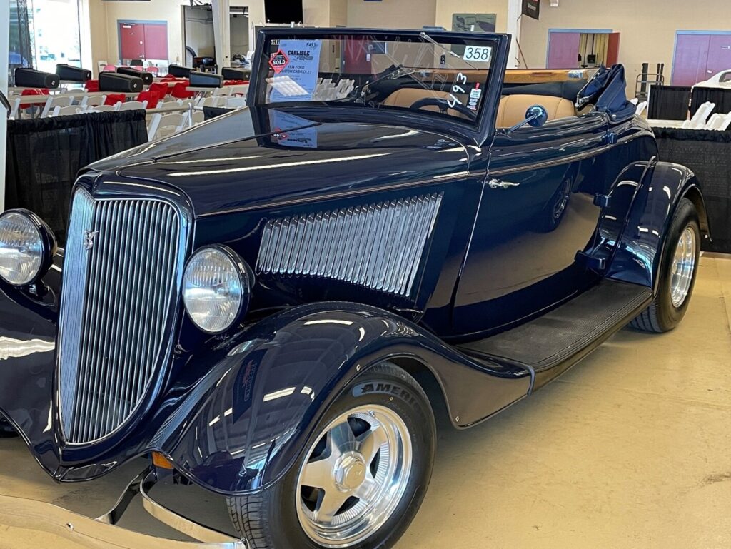 A blue Ford hot rod convertible at an auto auction inspecting a classic car before purchase