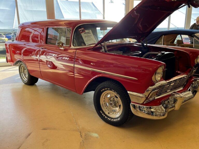 A man inspecting a classic car prior to a car auction; a red 55 Chevy panel wagon