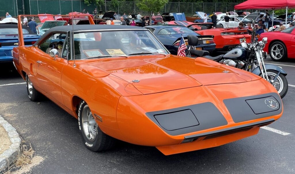 An orange with black vinyl top Plymouth Superbird at a car show after restoration using a car restoration contract