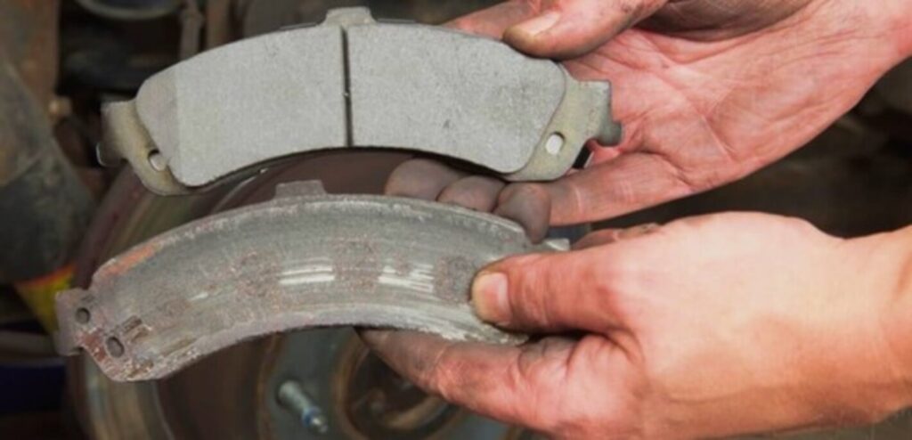 A person holding 2 car disk brake pads with 1 being new and the other being worn out