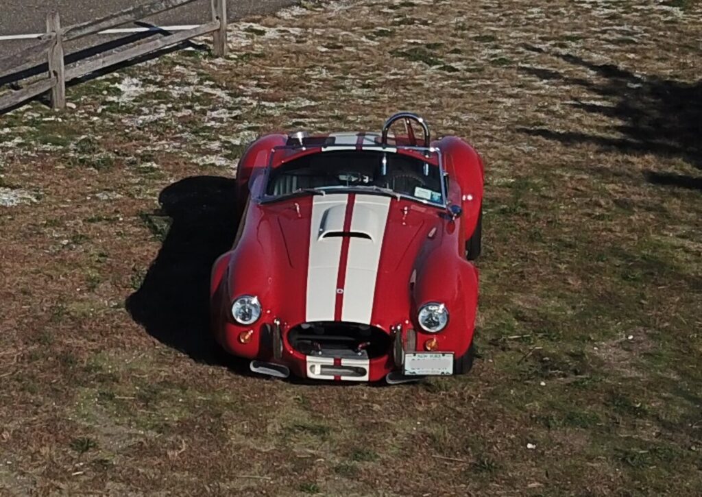 A red with white stripe AC Cobra parked in a field; deciding to switch to an automatic transmission