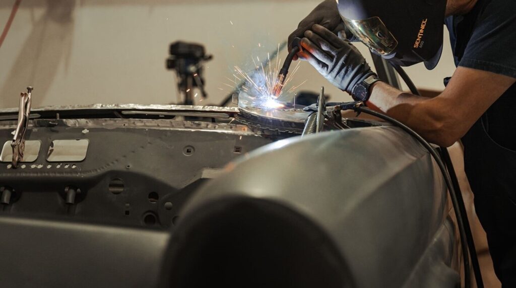 A mechanic working on welding repairs of the cowl of a classic car