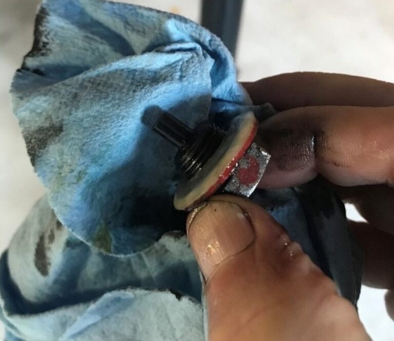A mechanic holding an oil drain plug and wiping with blue rag to check condition to avoid car engine problems