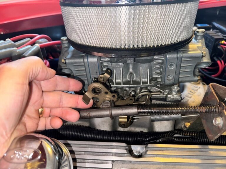A person moving the carb throttle linkage on a four barrel to make the car engine rev