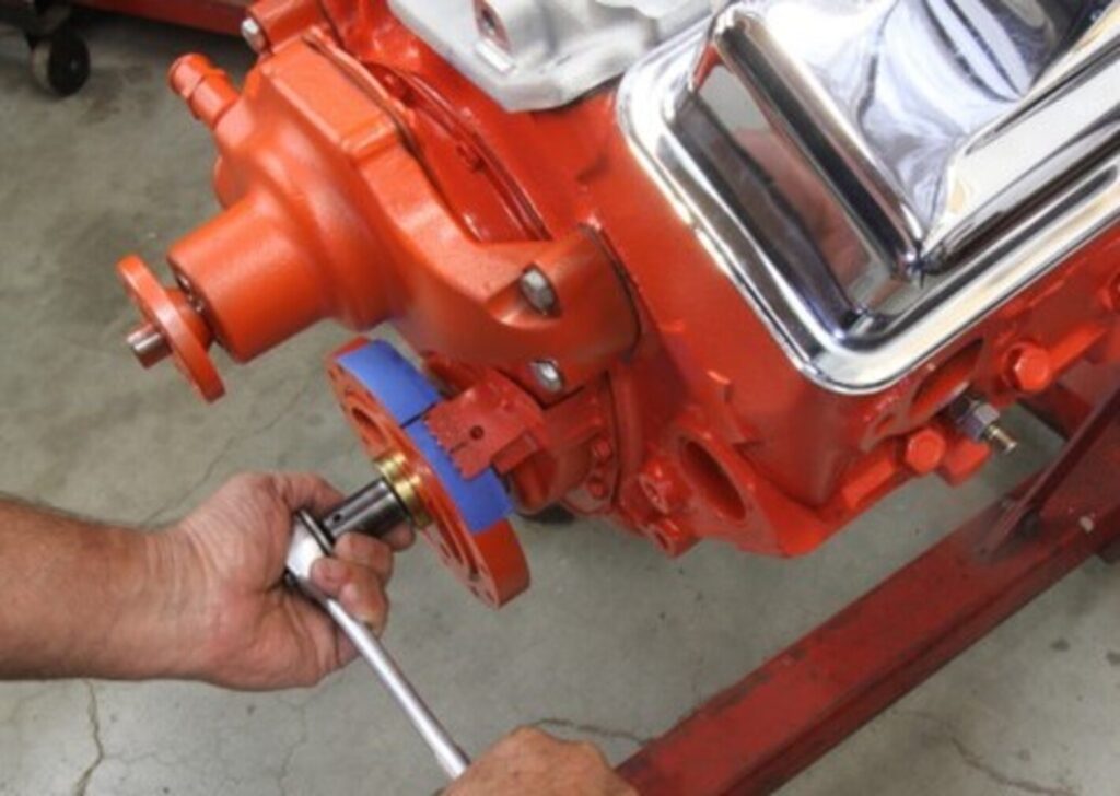 A mechanic using a silver wrench to rotate an orange Chevy engine to locate the engine's top dead center