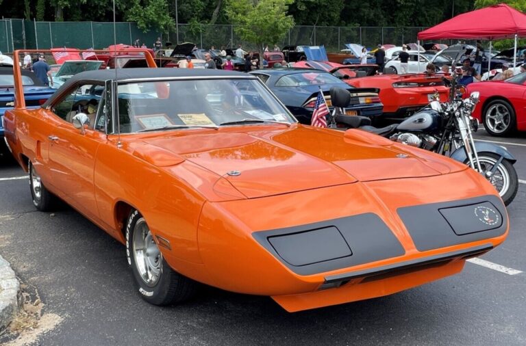 An orange with black vinyl top Plymouth Superbird at a car show as an example of an American muscle cars
