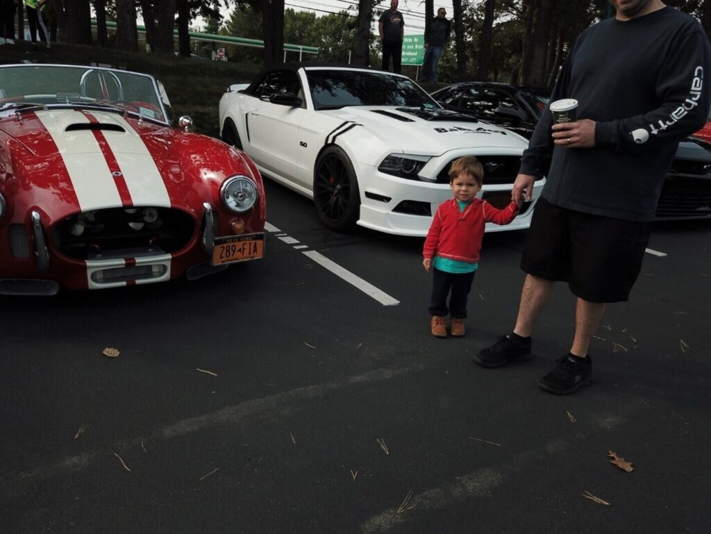 A father and son holding hands while looking a classic cars parked at a show as part of the vintage car hobby