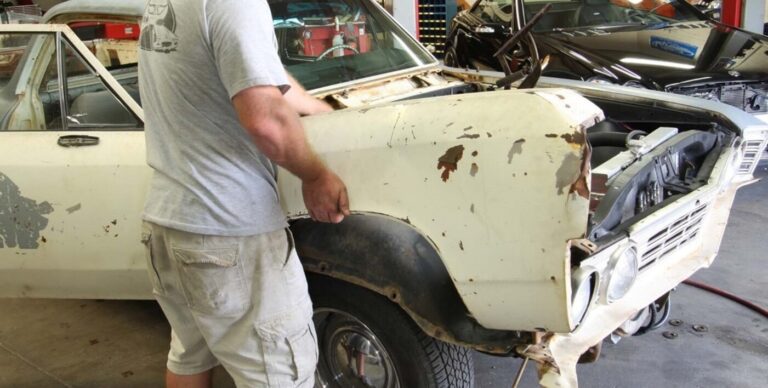 A car body shop worker placing a front right fender on a Chevrolet car as part of car resotration