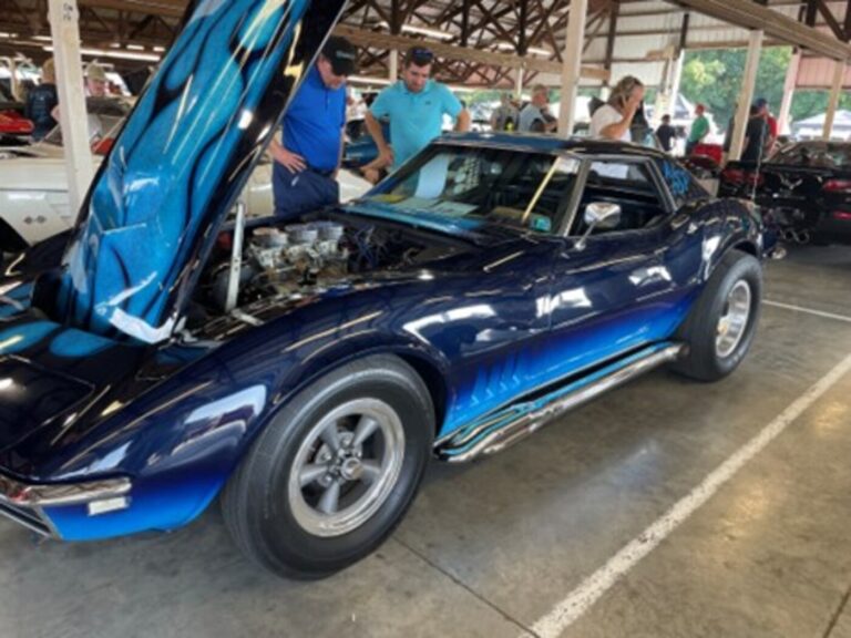A multi-color blue 1968 Chevy Corvette custom car with chrome side exhaust at a car show with 2 men look at the car's restoration direction