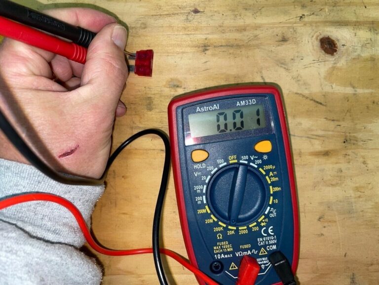 A mechanic using a multimeter car repair tool to check a car fuse condition
