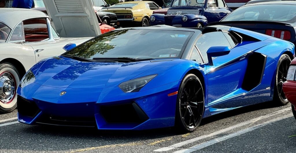 A bright blue Lamborghini at a classic car show next to a white Corvette as the future car collector