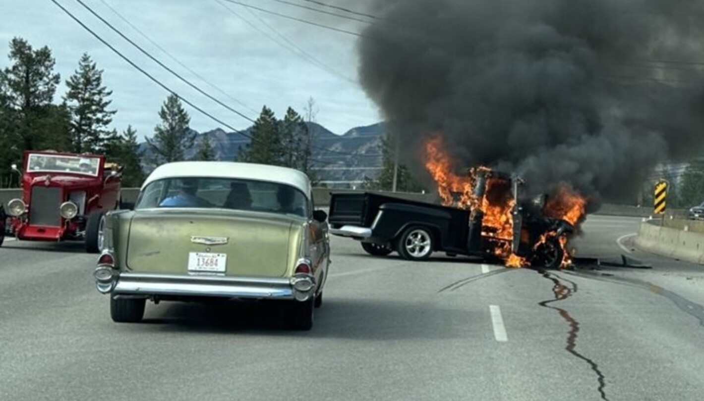 A vintage black truck on fire in the middle of the road with a green 57 Chevy and a roadster nearby requiring classic car insurance
