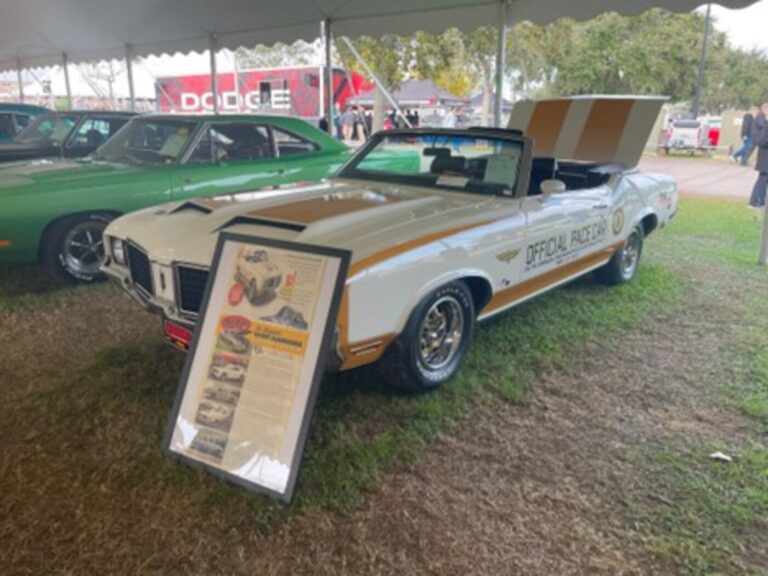 A white with gold stripes Oldsmobile Hurst Cutlass parked on grass at a classic car auction