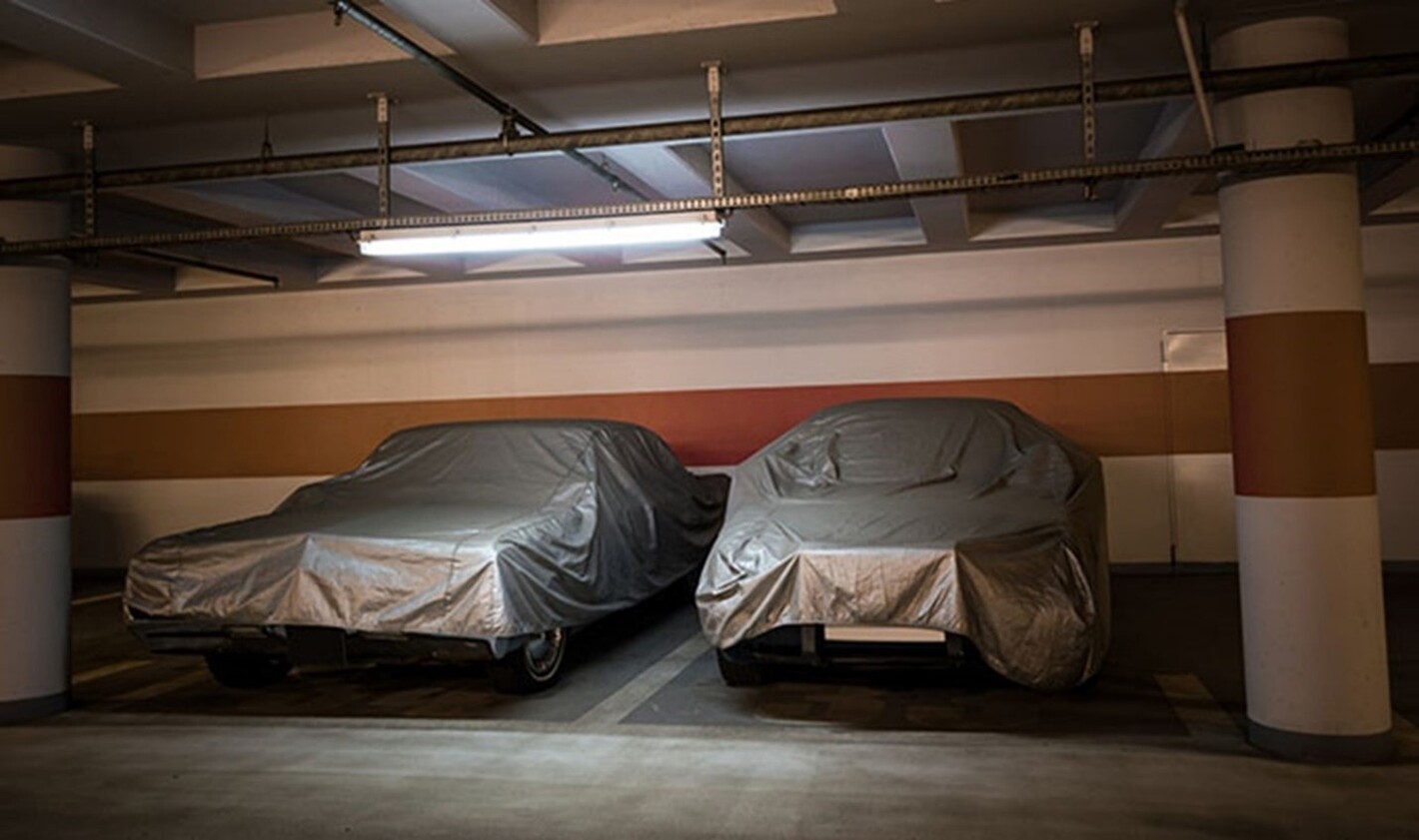 2 old cars prking in a garage under covers after vintage car winterizing