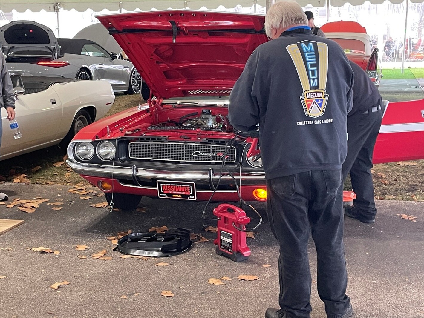 2 men working on a Red Challenger R/Y at a car show waiting on obtaining vintage car parts