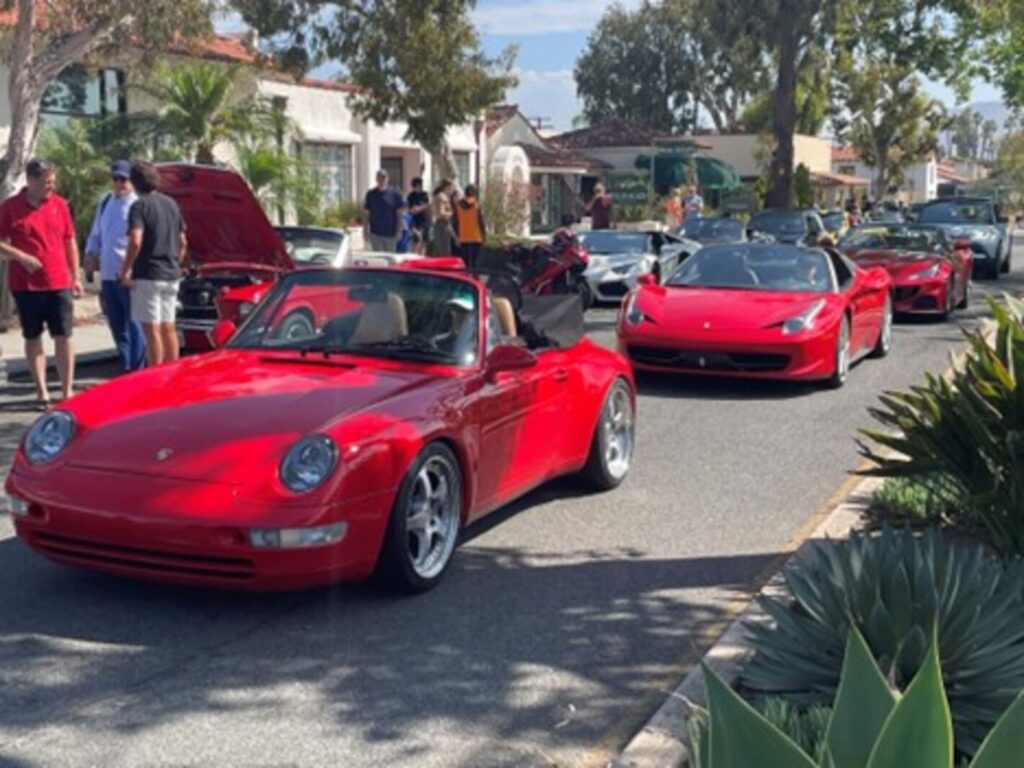 A group of red vintage cars on a California road for retires who enjoy classic cars including a Porsche, Mustang, and 2 Ferraris