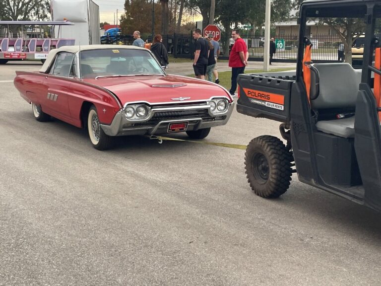 An ATV towing a red Ford Thunderbird down a road while waiting on vintage car parts