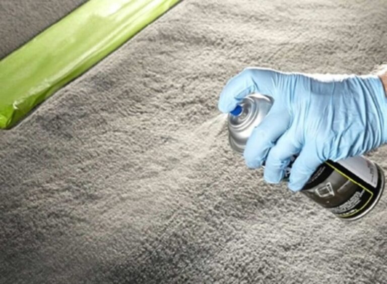 A man with a blue rubber glove spraying disinfectant on car carpet to remove interior odors