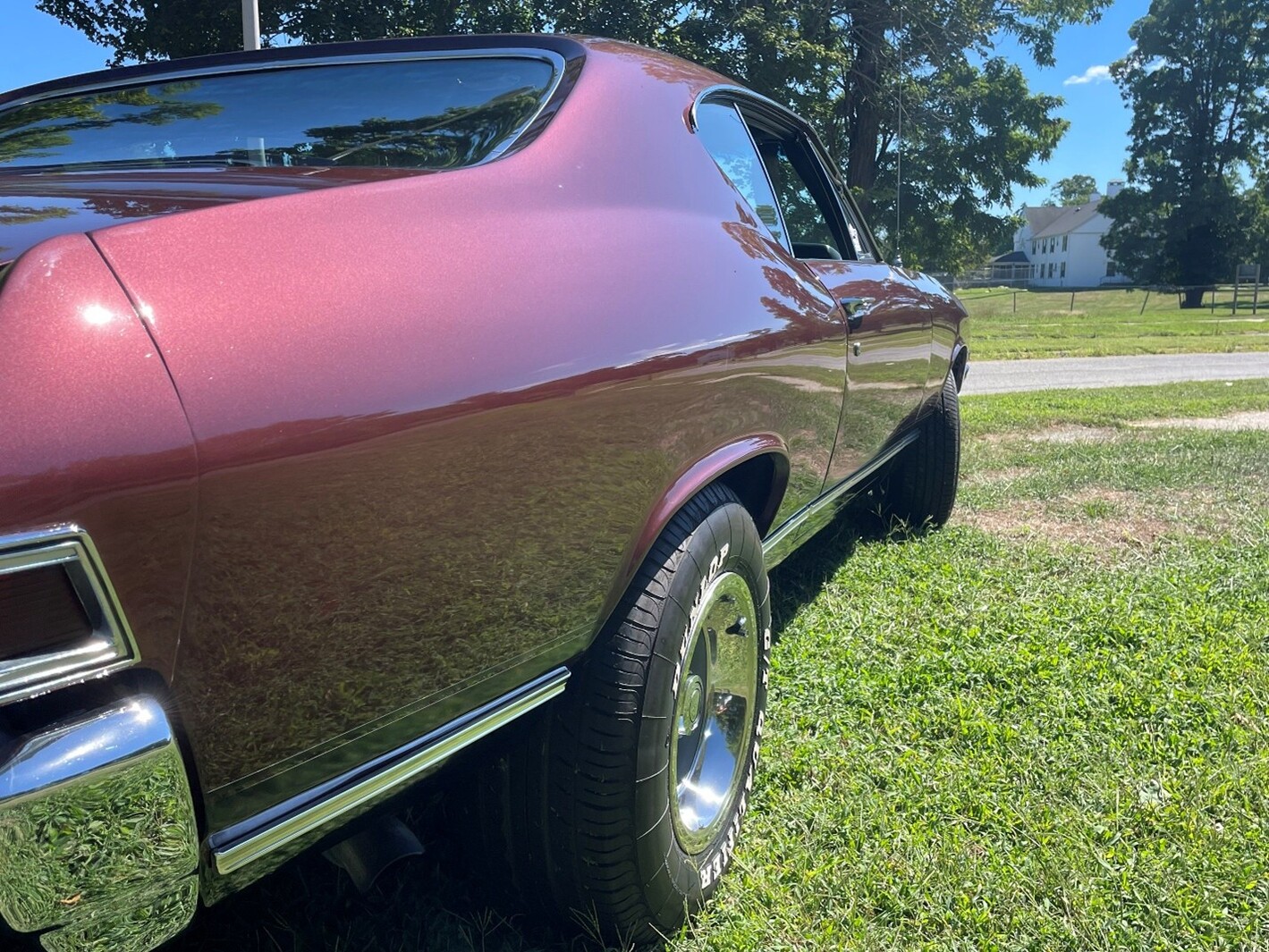 A left side view from the rear of the car of a maroon 1968 Chevy Chevelle parked on a lawn after using vintage car waxes